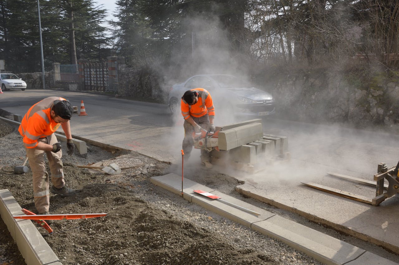 Workers cutting concrete on a road with a chainsaw, creating dust and working efficiently.
